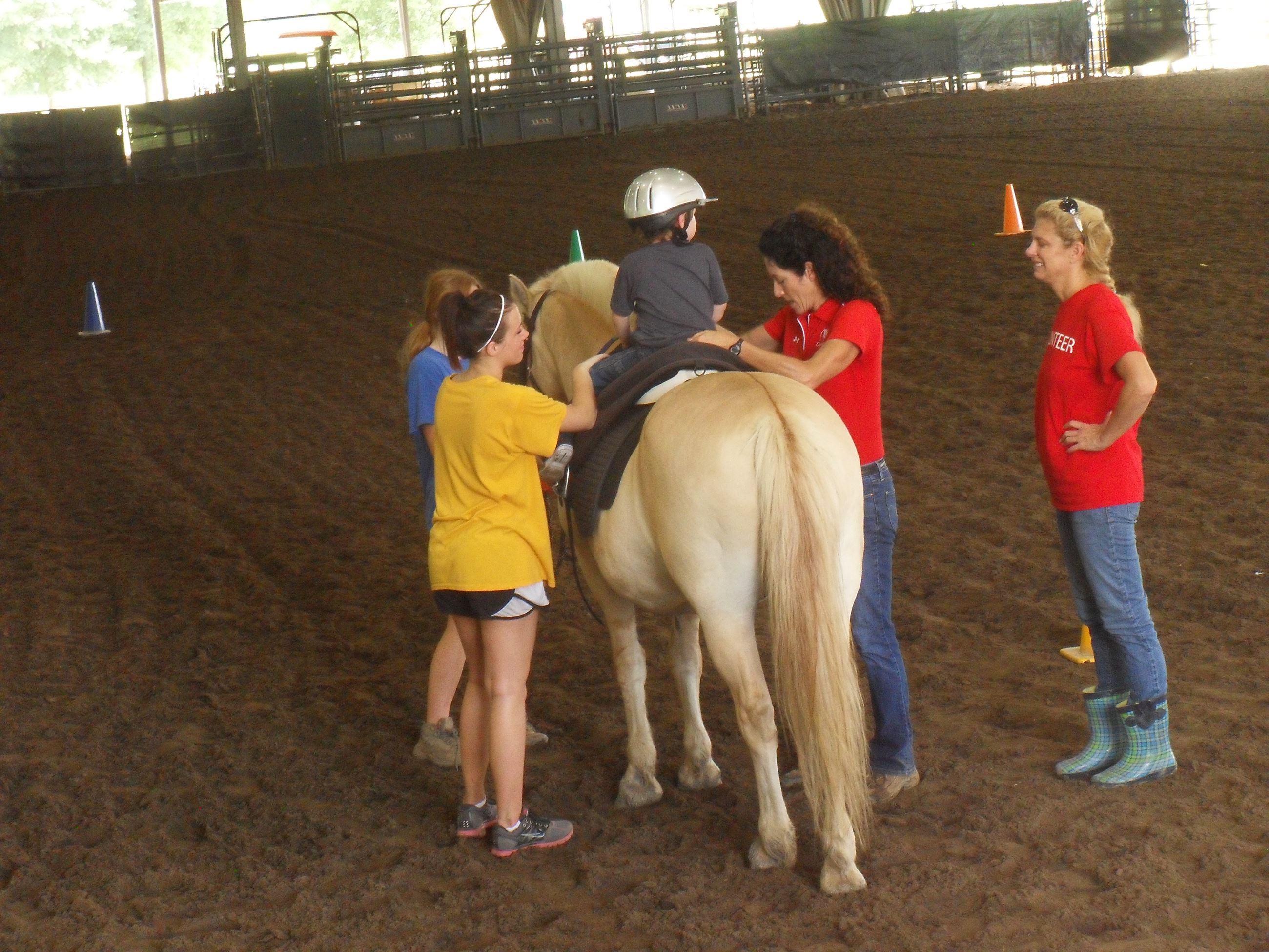 Child riding a horse with women walking it around the arena