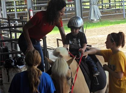 Three people help a child get seated on a saddle